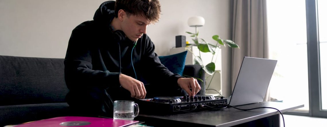 Een beginnende dj zit thuis achter zijn laptop te oefenen met zijn dj-controller.