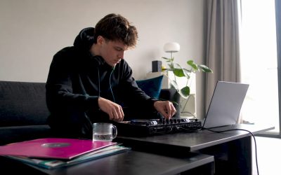 Een beginnende dj zit thuis achter zijn laptop te oefenen met zijn dj-controller.