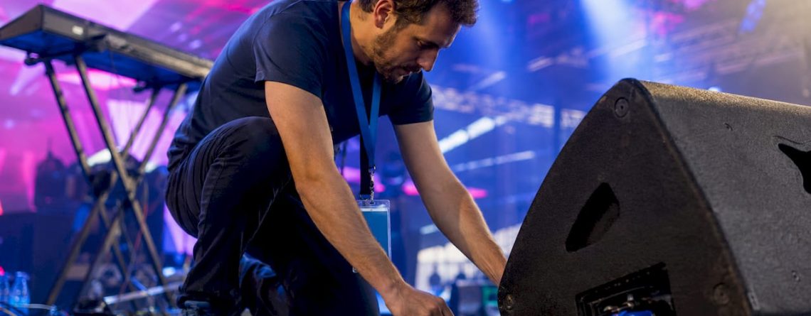 Een technicus plaatst een DI-box op het podium en zorgt dat alles goed aangesloten is.