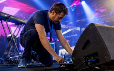 Een technicus plaatst een DI-box op het podium en zorgt dat alles goed aangesloten is.