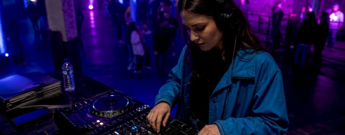 Een DJ staat met zijn koptelefoon op in de club en bereidt het volgende nummer voor.