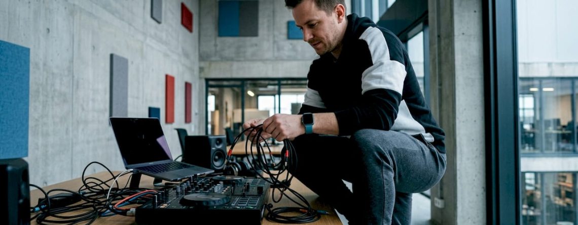 Een DJ is in zijn thuisstudio bezig met het netjes wegwerken en ordenen van alle kabels.