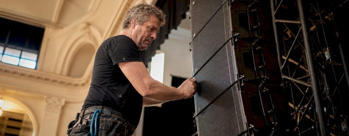 Een technicus is bezig met het installeren van een line array speakersysteem.