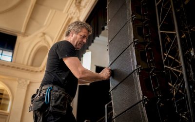Een technicus is bezig met het installeren van een line array speakersysteem.