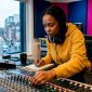 Een vrouw werkt achter een mengpaneel in een professionele opnamestudio.