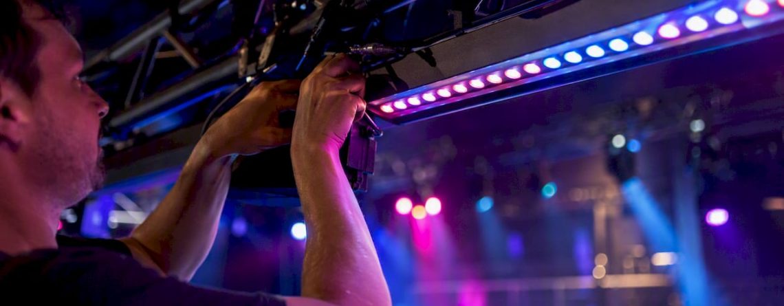 Een technicus bevestigt een LED-lichtbalk aan een trussconstructie.