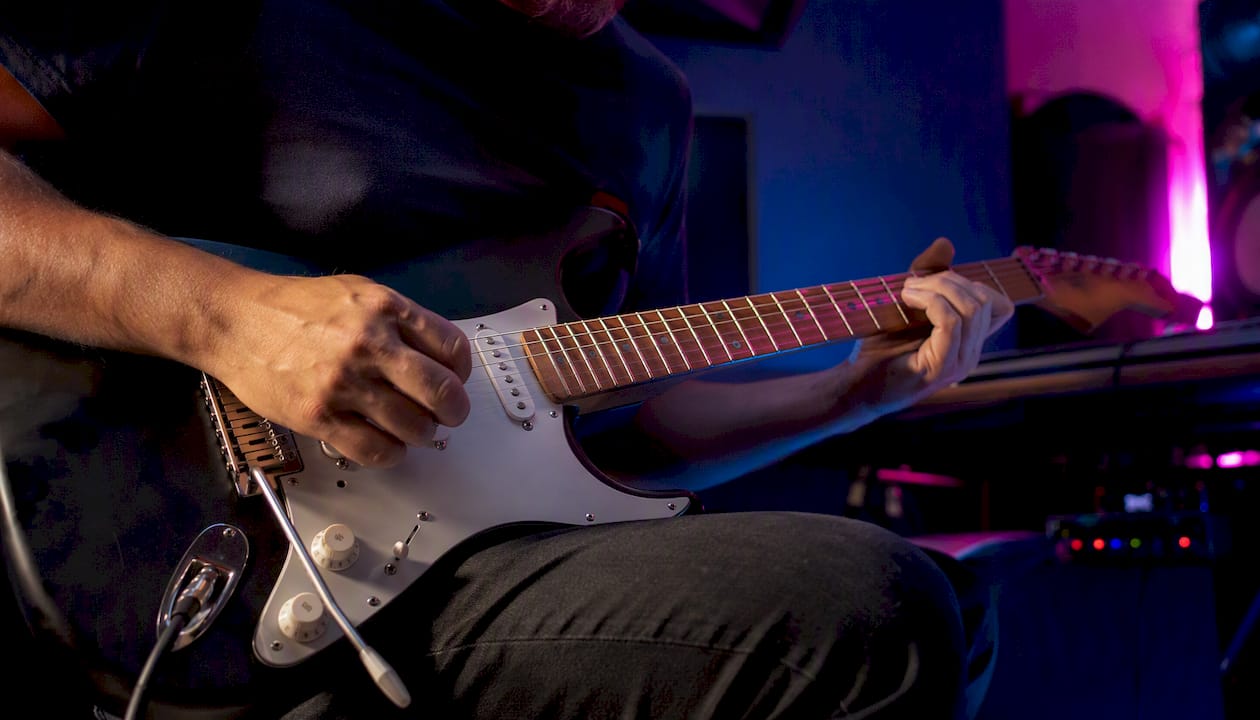 Een gitarist die in de studio een elektrische gitaar bespeelt.