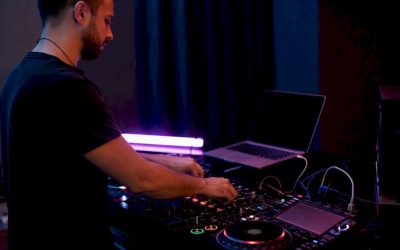 Handen van een dj die de mixer en koptelefoon afstellen in een donkere werkruimte