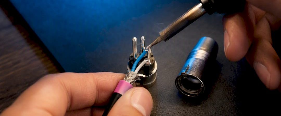 Handen die draden aan een XLR-connector solderen